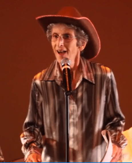 A man in a cowboy hat tells a story at a microphone
