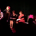 A group of performers on stage in a black box theater
