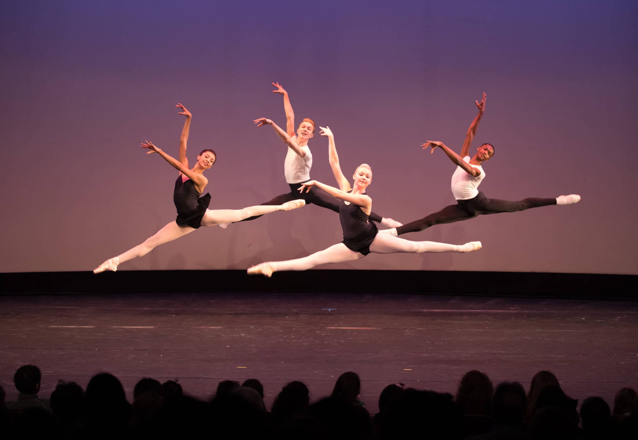 Photograph of four dancers in the air mid-leap