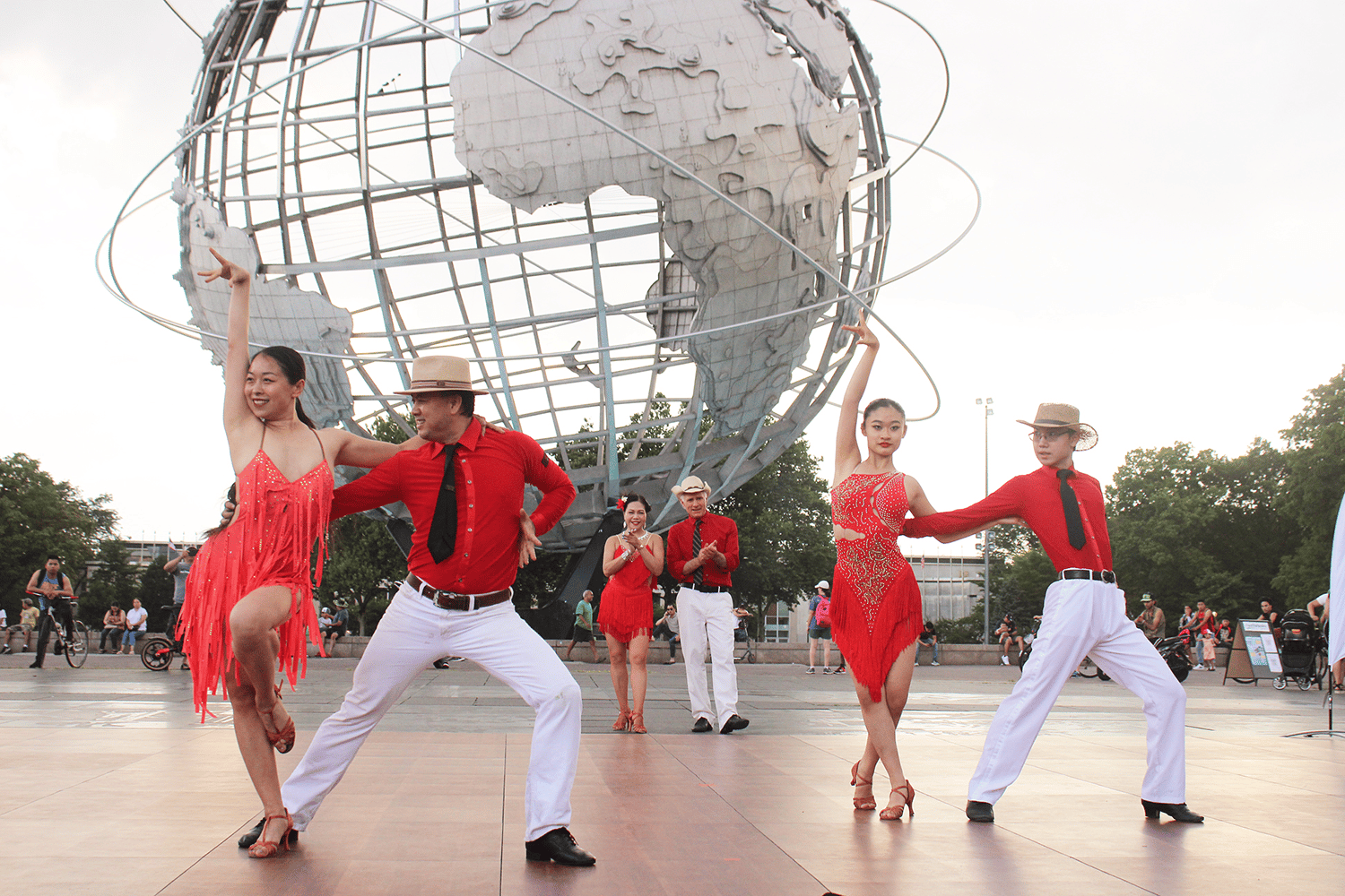 Dancers in red shirts and dresses performing in front of the Unisphere