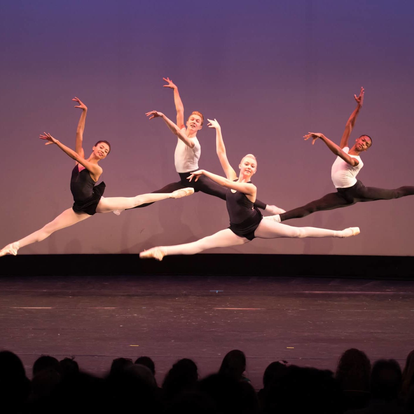 Photograph of four dancers in the air mid-leap