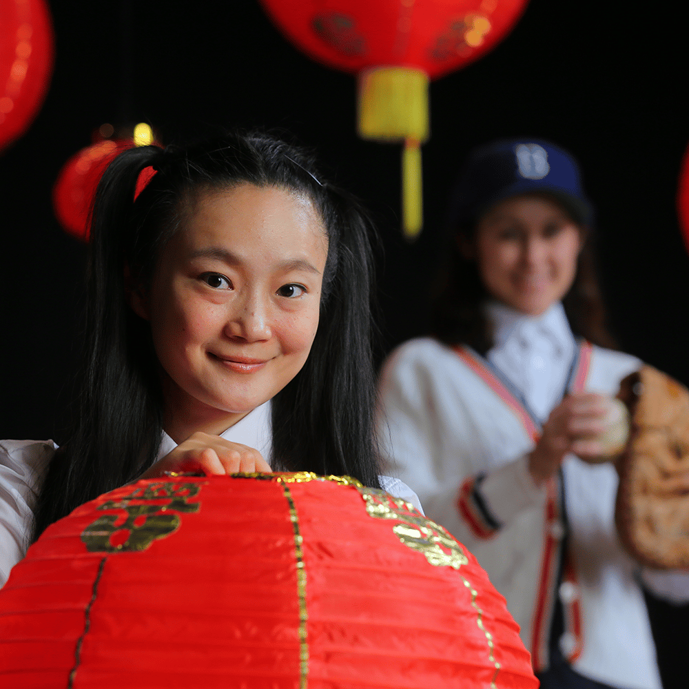 A girl with pigtail holds a red Chinese lantern with an out of focus person in a baseball uniform in the background